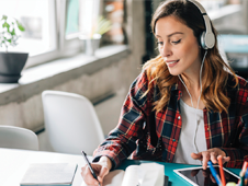 woman writing in a notebook with headphones on