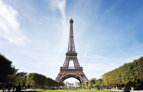 La tour Eiffel se dresse majestueusement sous un ciel bleu, entourée de jardins bien entretenus.