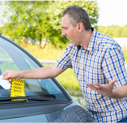 A man with an angry expression on his face picking up a notice placed on his car.