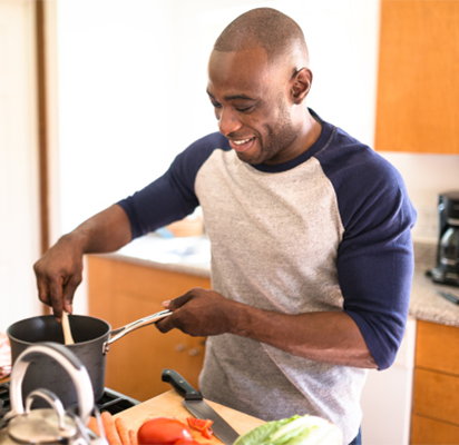 A man looking calm and smiling as he cooks in the kitchen.