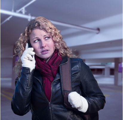 A woman looking at something behind her with fear as she holds her phone to the ear.